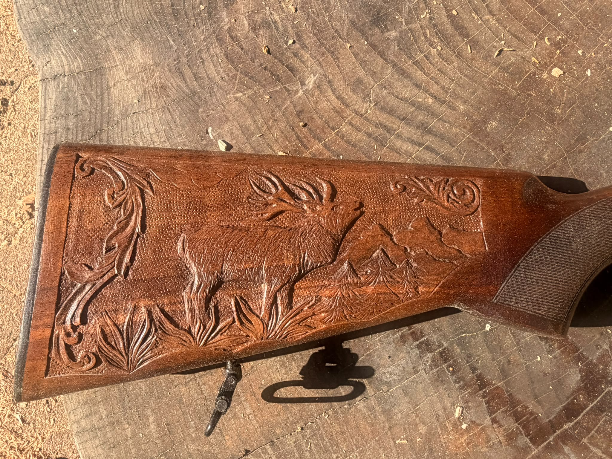 Crosse de fusil sculptée en relief : cerf brâmant devant un paysage de montagne et de sapins, encadré de rinceaux