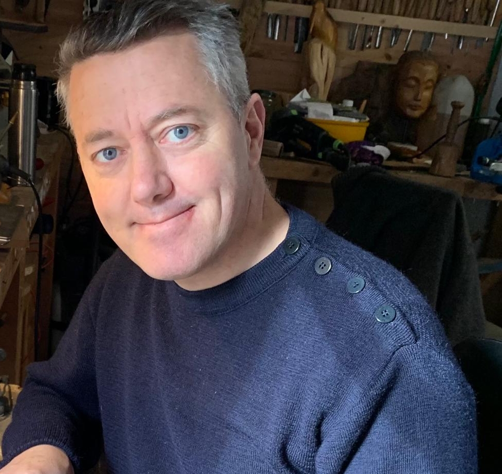 Portrait de Paul Crochat souriant dans son atelier, entouré de ses outils et de ses sculptures