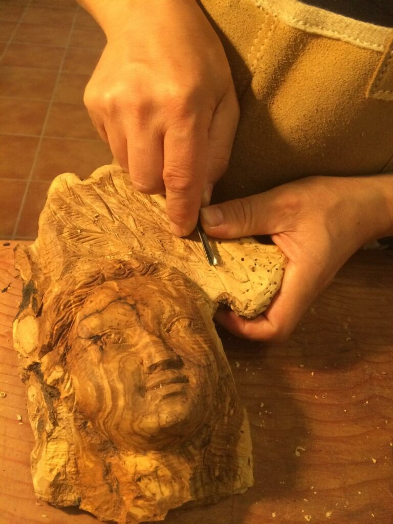 Mains sculptant à la gouge un visage dans une loupe de bois d’olivier