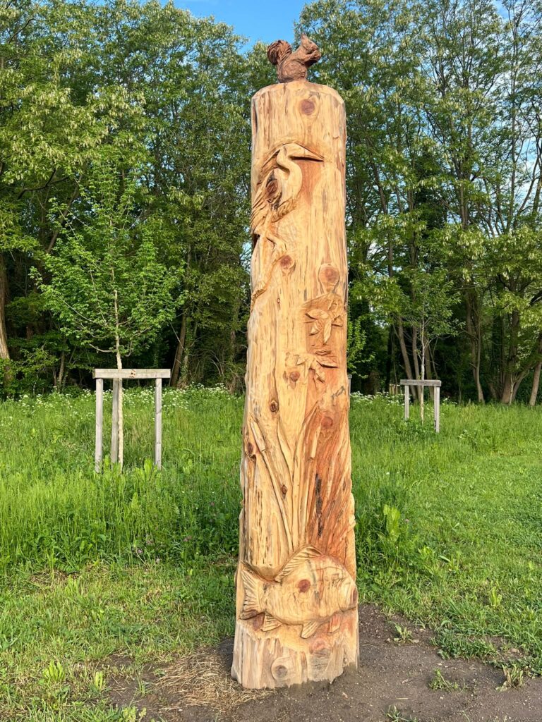 Colonne de bois sculptée d un héron, de poissons et d un écureuil, installée dans un espace vert public